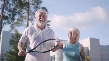 Güneşli bir günde tenis oynayan mutlu yetişkin çift. Yaşlı bir adam ve olgun bir kadın oyun keyfini çıkarın. Açık havada eğlence ve eğlence.