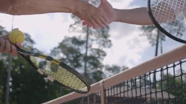 Närbild på äldre par som skakar hand efter att ha spelat tennis på tennisbanan. Aktiv fritid utomhus. Senior man och kvinna ha kul tillsammans — Stockvideo