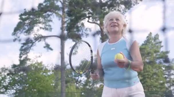 Framgångsrik lycklig mogen kvinna vann tennisturnering. Den gamla damen hoppar höjer händerna med racket i en vinnande gest. Aktiv fritid utomhus — Stockvideo