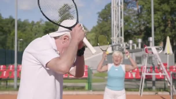 Üzgün olgun çift tenis kortu turnuva kaybetti. Kıdemli adam ve kadın elleri raketleri tutan başını tutuyor. Açık havada aktif boş zaman. Yenilgi kavramı — Stok video