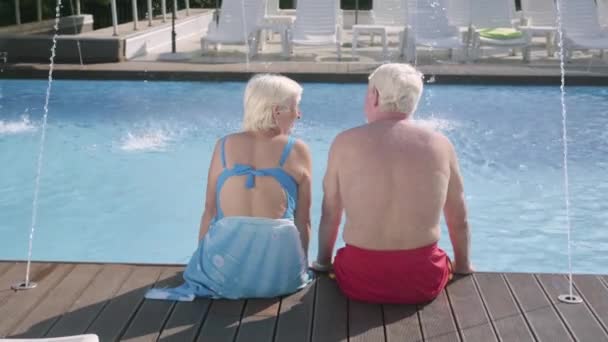 坐在泳池边上的快乐成熟夫妇的后视图。可爱的老年男人和女人在酒店大楼里放松。幸福友好的家庭. — 图库视频影像