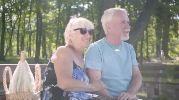 Glückliches älteres Paar, das auf der Bank sitzt und die Natur bewundert. Senior Mann und Frau entspannen zusammen. Freizeit im Freien — Stockvideo