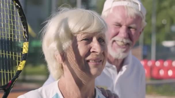 Porträtt äldre par som spelar tennis en solig dag. En gammal man och en mogen kvinna njuta av spelet. Rekreation och fritid utomhus. — Stockvideo