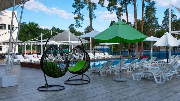 Henge kurvstoler og svømmebasseng og parasoller på fritidssenteret om sommeren. Fritidsaktiviteter og fritid utendørs. Luksushotell . – stockfoto