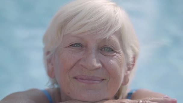 Крупним планом портрет зрілої усміхненої сіро-волохатої жінки, що плаває в басейні. Відпочинок та дозвілля на відкритому повітрі . — стокове відео