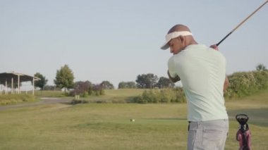 Omzunda dövme ile genç konsantre orta doğu adam golf sahasında golf oynarken. Yakışıklı adam bir golf kulübü kullanarak ve uzağa bakarak topa vurdu. Yaz eğlence