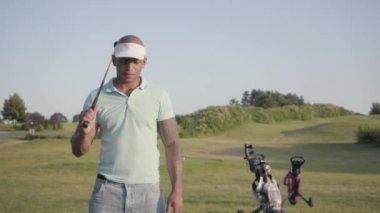 Bir golf sahası iyi güneşli havalarda kamera bakarak duran bir golf kulübü ile gülümseyen bir emin başarılı orta doğu adam Portresi. Spor ve eğlence açık havada.