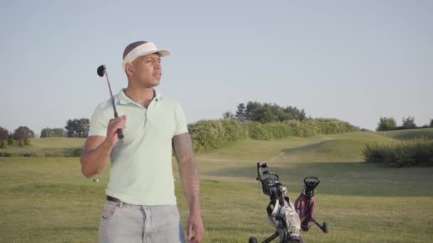 Portrét roztomile usměvavý, úspěšný muž středního východu s golfovým klubem, který stojí na golfovém hřišti za dobrého slunečného počasí. Sport a volný čas venku. — Stock video