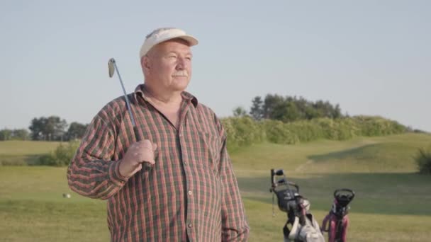 Portrét sebevědomého úspěšného dospěla s golfovým klubem, který stojí na golfovém hřišti za dobrého slunečného počasí. Sport a volný čas venku. — Stock video