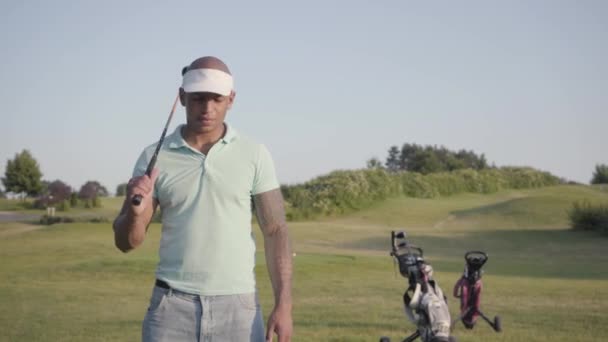 Retrato de um sorridente confiante bem sucedido homem do Oriente Médio com um taco de golfe em pé em um campo de golfe olhando para a câmera em bom tempo ensolarado. Desporto e lazer ao ar livre . — Vídeo de Stock