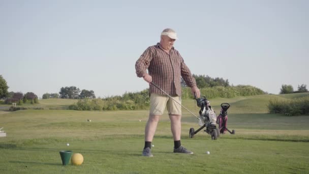 Starší muž se před zápasem zahřívá a drží golfový klub přes hlavu. Starý pán hraje hru venku. Letní čas — Stock video