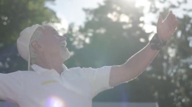 Sevimli kendine güvenen başarılı gülen olgun adam tenis kortu tenis oynarken. Yaşlı adam raketle topu atıyor. Açık havada aktif boş zaman. Yavaş çekim.