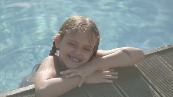 Schattig grappig meisje in gele zonnebrillen op zoek in de camera glimlachend, kijkend uit het zwembad, vasthouden aan de rand. Kind plezier in het hotel complex. Recreatie en vrije tijd buiten. Slow Motion — Stockvideo