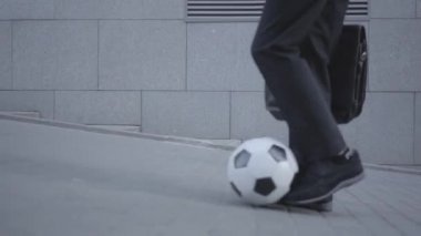 İyi giyimli bir çocuğun ayakları sokakta topa önderlik edip çantayı tutuyor. Ciddi genç adam aynı anda çocuk ve yetişkin gibi davranıyor. Alt görünüm