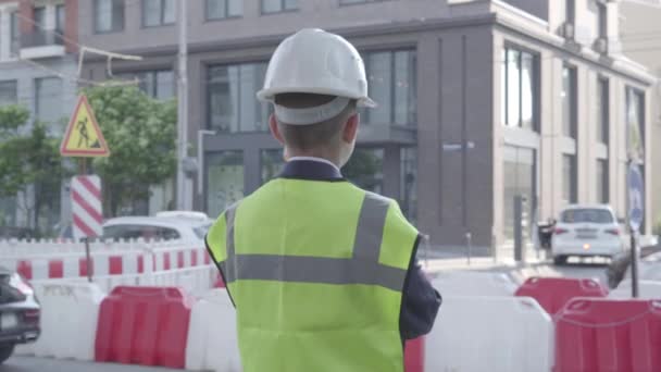 Malý chlapec nosí pracovní kombinézu, bezpečnostní výstroj a konstruktér, který stojí na rušné silnici ve velkém městě. Inženýr, architekt, Tvůrce své práce. Dítě jako dospělý. — Stock video