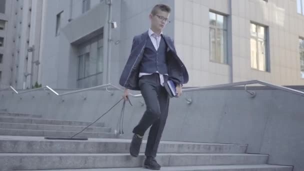 Schattige kleine jongen het dragen van een Business Suit houdt boeken in zijn handen en trekt een computer keyboard snoer. Kind als volwassene. — Stockvideo