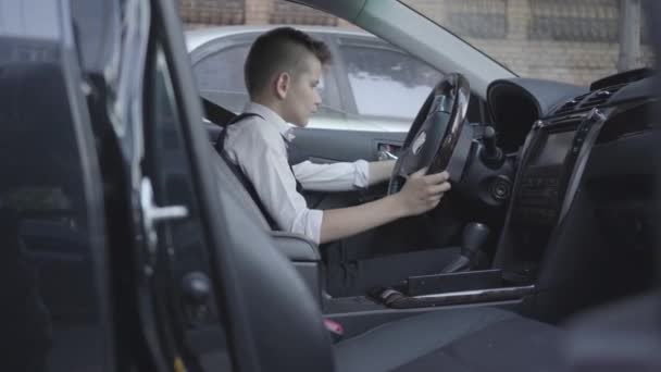 Menino bonito em terno de negócios sentado no carro estudando o salão. Criança como adulto . — Vídeo de Stock
