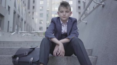 Sokakta merdivenlerde oturan pensive iyi giyimli sevimli çocuk. Çocuk yorgun ve sadece bir çocuk olmak istiyor. Bir yetişkin olarak çocuk.