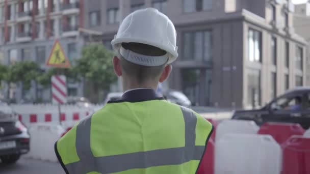 Little boy wearing business suit and safety equipment and constructor helmet standing on a busy road in a big city. Engineer, architect, builder doing his work. Child as adult. — Stock Video