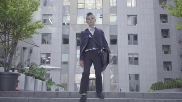 街を歩くケースでビジネススーツを着たかわいい男の子。大人の子供. — ストック動画