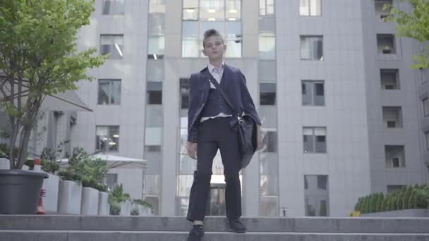 Lindo niño vistiendo un traje de negocios con estuche caminando por la ciudad. Niño como adulto . — Vídeo de stock