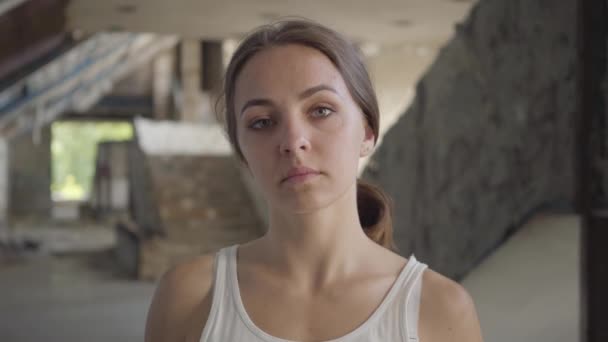 Retrato de uma jovem atraente colocando um boné militar na cabeça e olhando para a câmera em pé no prédio abandonado. O conceito de uma menina forte, mas feminina. Tempo de guerra — Vídeo de Stock