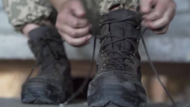 Zblízka v rukou mladé ženy v vojenské uniformě, která sedí na studených betonových schodech v opuštěné budově, a rozvazuje staré boty, připravující se na trénink. Koncept silné dívky — Stock video