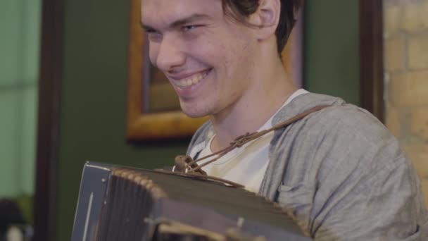 Geschicklichkeit junger Mann auf dem Akkordeon lächelnd. Fröhliche Musik auf dem alten Instrument. Volkskonzept — Stockvideo