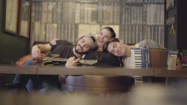 Bearded man met gitaar en zijn vriend met accordeon zetten hun hoofden op de borst van een vet meisje zittend op de zijkanten van haar. Ontspanning in de pub. Vrienden plezier samen — Stockvideo