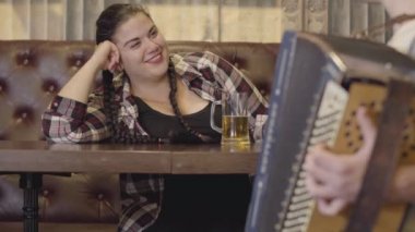 Tanınmaz adam akordeon oynarken çekici tombul kadın bira içme ve onu hava öpücük göndererek. Rus geleneksel müzik kavramı. Halk konsepti