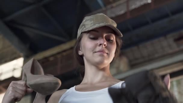 O retrato da menina escolhe entre botas militares e sapatos de salto alto elegantes no edifício abandonado. Mulher infeliz leva botas e se preparando para o treinamento. O conceito de guerra e paz. Vista inferior — Vídeo de Stock