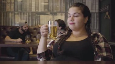 İki erkek arka planda alkol İçirken bir bardak bira ile Bar tezgahında oturan pigtails ile tombul kadın. Erkekler ve kadın birbirlerine flört bakıyor