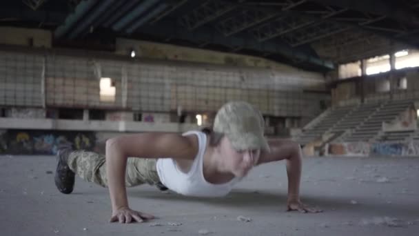 Giovane donna in uniforme militare che si avvolge dal pavimento su un pavimento di cemento in un edificio abbandonato. Una donna si allena prima di combattere. Il concetto di una donna forte — Video Stock