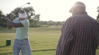 Yakışıklı Orta Doğu golfçü sallanan ve güzel ders Golf topu vurmak. Yaşlı bir adam rakibini izliyor ve beş verir. Açık havada rekreasyon ve spor konsepti.