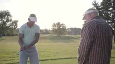 Yakışıklı Orta Doğu golfçü sallanan ve güzel ders Golf topu vurmak. Yaşlı bir adam rakibini izliyor.