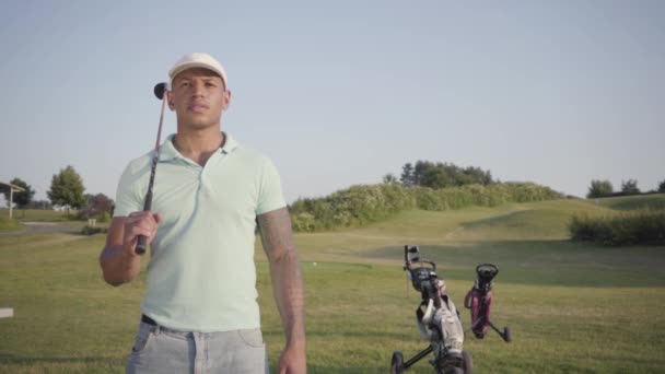 Un giovane uomo mediorientale concentrato distoglie lo sguardo con la mazza da golf sulla spalla. Un bell'uomo che gioca a golf sul campo da golf. Tempo libero estivo. Rallentatore — Video Stock