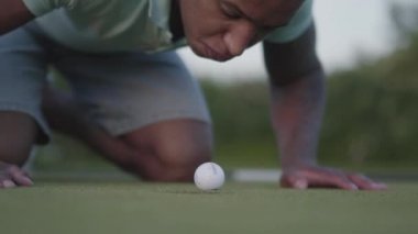 Golf sahasında golf oynayan genç Orta Doğulu adam. Yakışıklı adam sonbahar yapmak için çalışıyor delik kenarında yatıyor Golf topu üfleme. Açık havada rekreasyon ve spor konsepti.