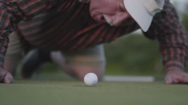 Volwassen man probeert te blazen een golfbal in het gat. Het concept van recreatie en sport buitenshuis. — Stockvideo