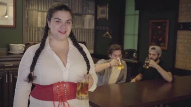 Beyaz bluz ve korse tutan bira cam arka planda alkol içme iki erkek doğru bakıyor pigtails ile tombul kadın. Barda boş zaman.