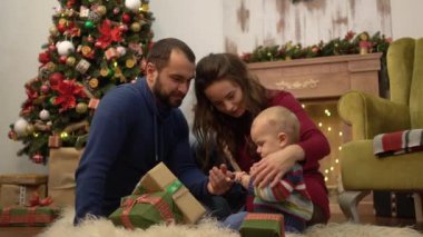 Sevimli eğlenceli aile Noel birlikte anne, baba ve küçük bebek Noel dekorasyonu ile odada yerde oturan kutluyor. Çocuk mevcut hediye kutuları ile oyun kabarık üzerinde yatıyor