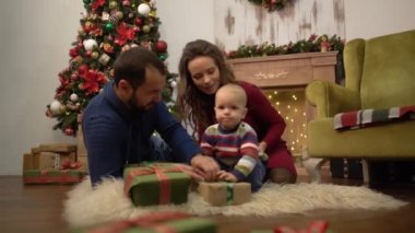 Mutlu aile Noel birlikte Noel dekorasyon ile odada yerde oturan anne, baba ve küçük bebek kutlamak. Çocuk mevcut hediye kutuları ile oyun kabarık halı üzerinde yatıyor.