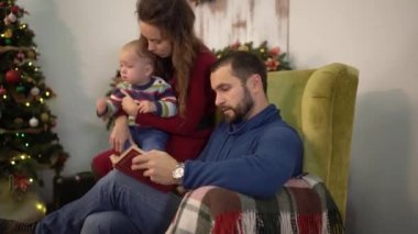 Mutlu sevimli aile birlikte kitap okuma zaman harcamak. Baba koltukta oturuyor, küçük bebek oğlunu kucağına tutuyor, Anne kolçak üzerinde oturuyor, gülümsüyor. Mutlu aile boş