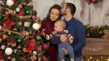 Anne, baba ve bebek Noel dekorasyonu ile odada eğlenmek. Babam ve annem çocuğla oynuyorlar, onu kollarda tutarak atar. Mutlu aile birlikte Noel kutluyor