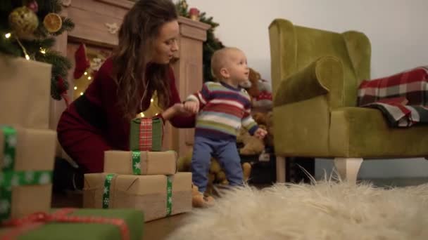 Linda madre alegre alegre y el bebé pasan su tiempo libre al lado del árbol de Navidad en casa . — Vídeos de Stock