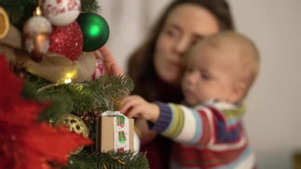 Madre, padre e piccolo bambino che decorano il nuovo albero di Capodanno primo piano. Donna che tiene il bambino vicino all'abete, mostrando decorazioni luminose, giocattoli appesi all'uomo. Felice famiglia che celebra il Natale insieme — Video Stock