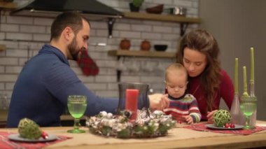 Anne, baba ve bebek modern mutfakta eğleniriz. Baba ve anne çocuk ile oynarken, adam bir çocuk eğlendirmek için masada yuvarlak şeker Spinning. Mutlu aile birlikte zaman harcamak