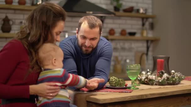 Mère, père et un bébé s'amusent dans la cuisine moderne. Papa et maman jouent avec l'enfant, homme demandant garçon de partager des bonbons avec lui. Bonne famille passer du temps ensemble — Video