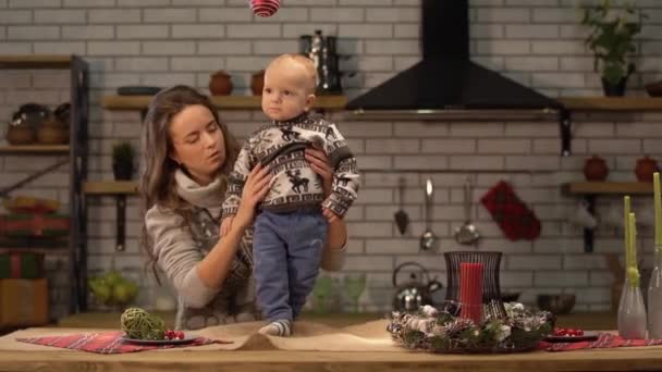 Jolie jeune femme et bébé mignon dans ses bras debout dans la cuisine moderne. Concept de famille heureuse . — Video