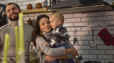 Sıcak kazak içinde sakallı baba mutfakta anne silah olan bebek küçük oğlu ile oynuyor. Çocuk adam tekme ve yüzünü kapmak için çalışan, Anne gülümseyen. Mutlu dost aile birlikte zaman harcamak