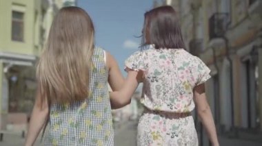 Alışveriş çantaları ile iki yürüyen kadınların arka görünümü. Genç kızlar vakit geçirmek ile zevk şık yazlık elbiseler giyiyor. Alışveriş yaşam tarzı kavramı. Yavaş hareket.